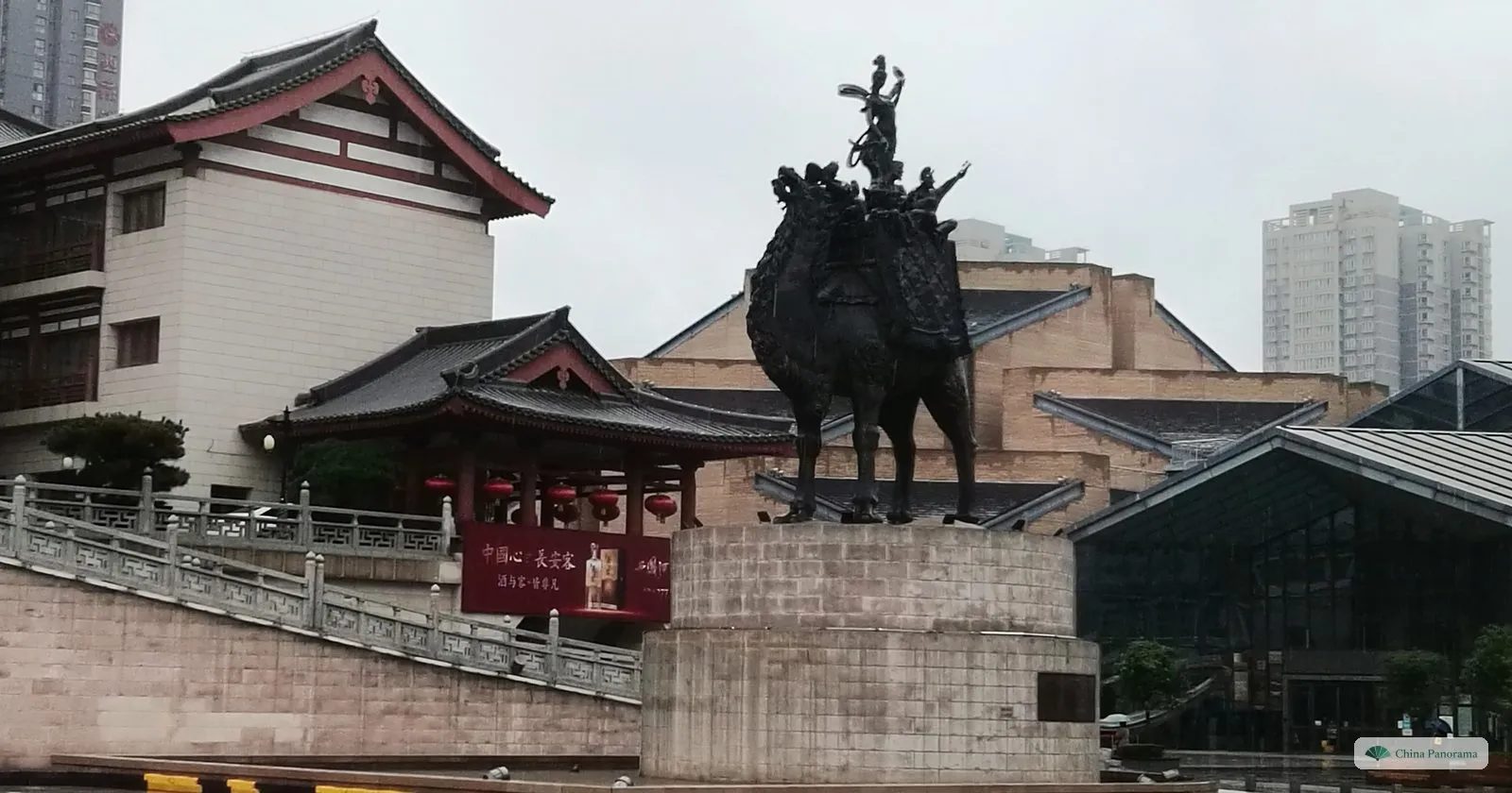 A bronze camel carrying a group of musicians on its back, on a stone plinth in front of the halls of Tang West Market
