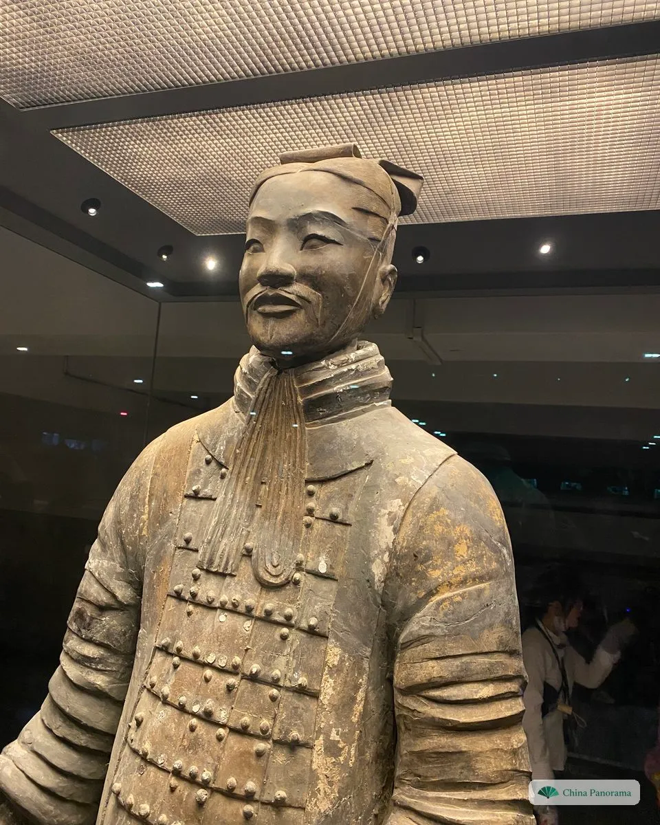 A terracotta officer in a glass case, seen from the chest up: a flat cap tied under the chin, a moustache and scaled armour with traces of colour