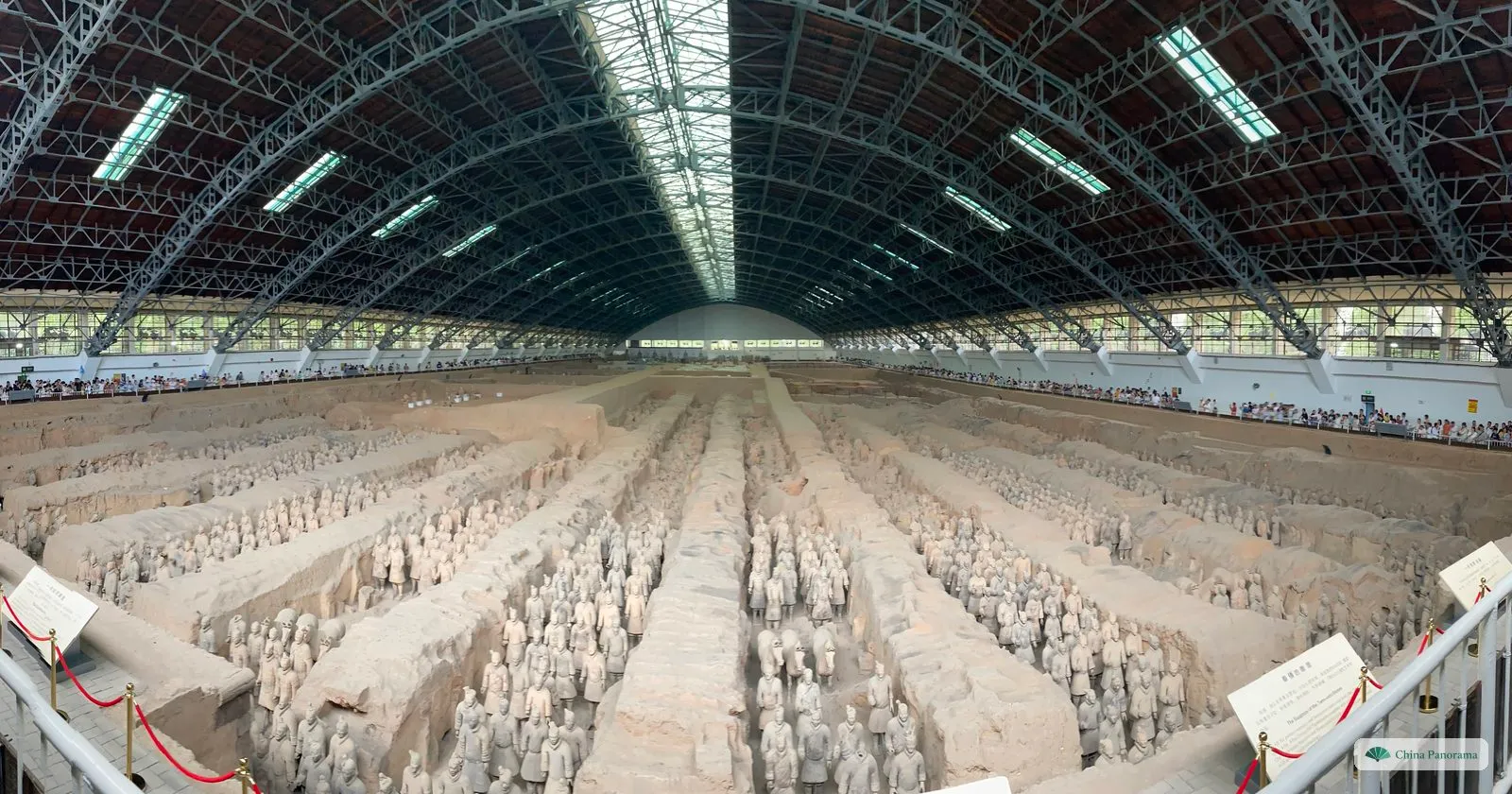 Pit 1 of the Terracotta Army under its arched steel roof: rows of clay soldiers standing in long corridors between earth walls, with visitors lining the gallery on both sides