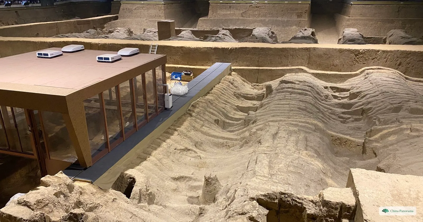 The excavation of Pit 2: wavy ridges of collapsed roof timbers in the earth, with a glass-walled laboratory built into the pit on the left