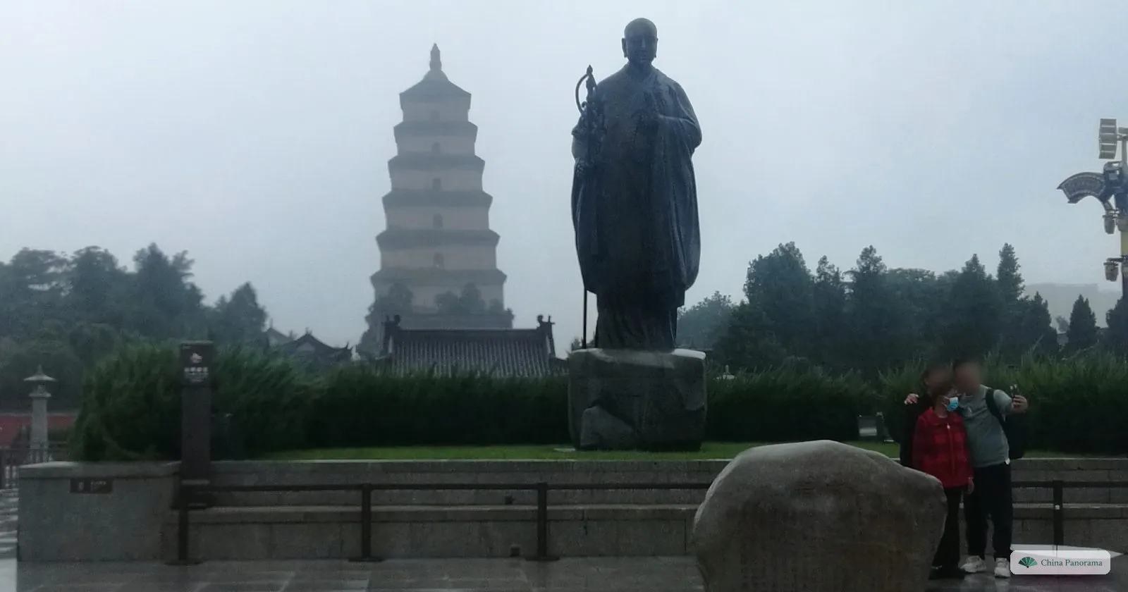 The bronze statue of the monk Xuanzang, staff in hand, on the South Square in front of the Giant Wild Goose Pagoda on a misty, rainy day