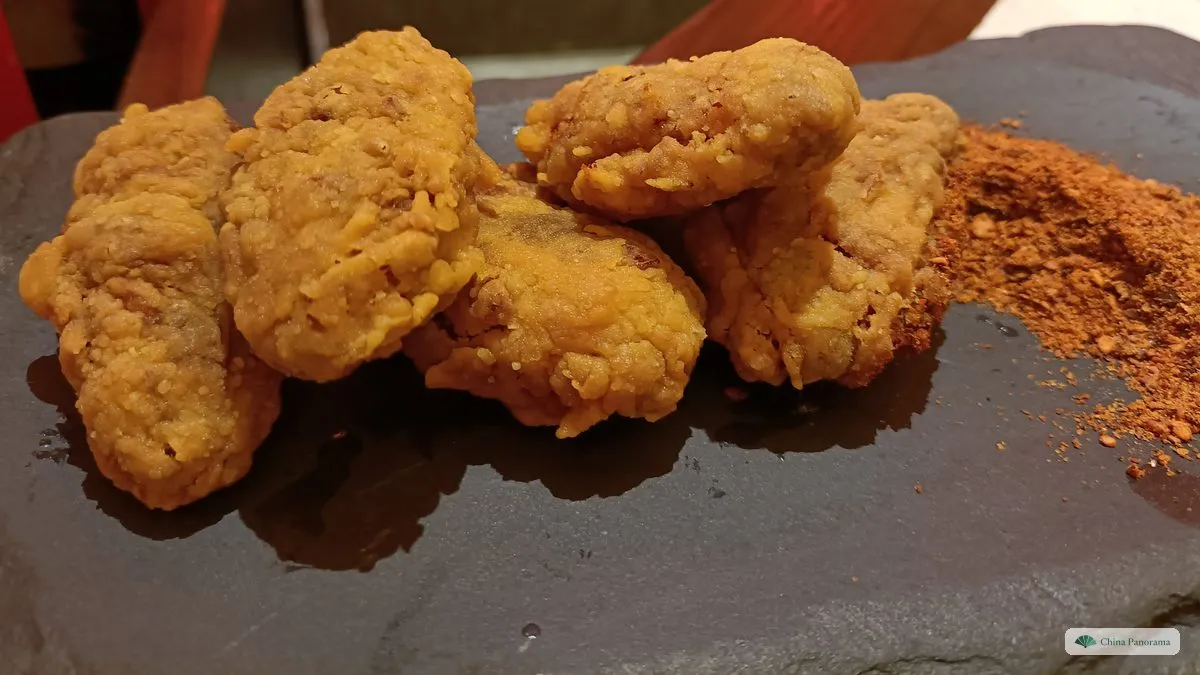 Golden, crumbly fried pork pieces on a dark stone plate, next to a small heap of red chilli powder