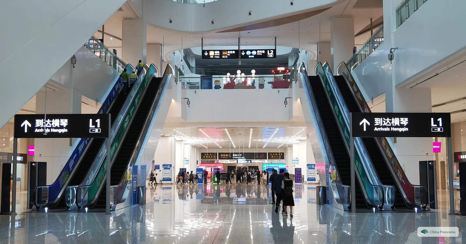 The arrivals hall of Hengqin Port: two pairs of escalators under black signs “Arrivals Hengqin” in a bright white hall
