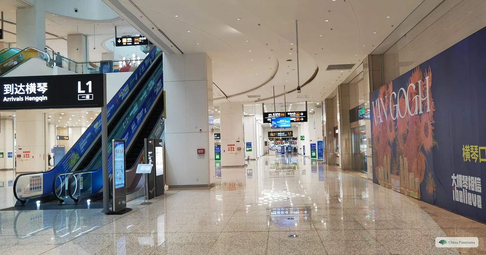 A wide, almost empty arrivals hall with an escalator under a sign “到达横琴 Arrivals Hengqin” and a large Van Gogh exhibition poster on the right
