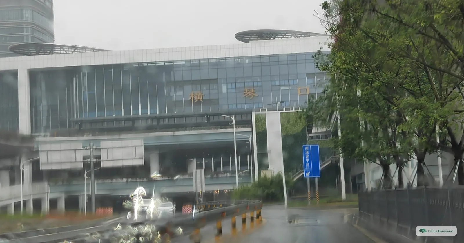 A large glass building with gold characters on its facade and saucer-shaped roof canopies, seen through a rain-streaked windscreen