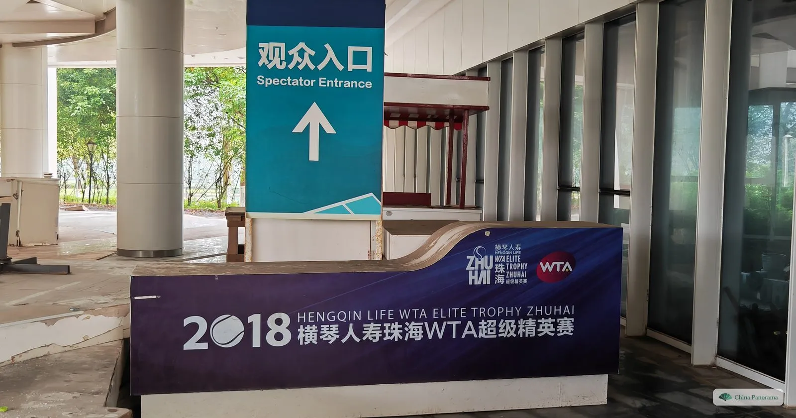 a purple sign reading “2018 Hengqin Life WTA Elite Trophy Zhuhai” under a teal post marked “Spectator Entrance” in an empty concourse