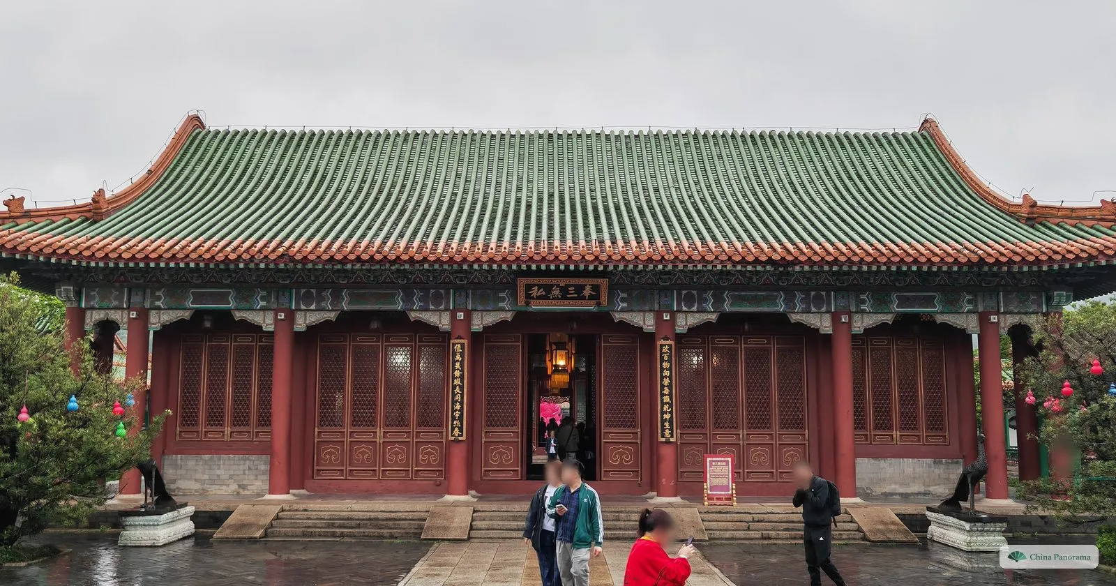 A hall with a sweeping green glazed roof and a dark plaque 奉三无私 over red lattice doors, bronze animals on pedestals and a few visitors