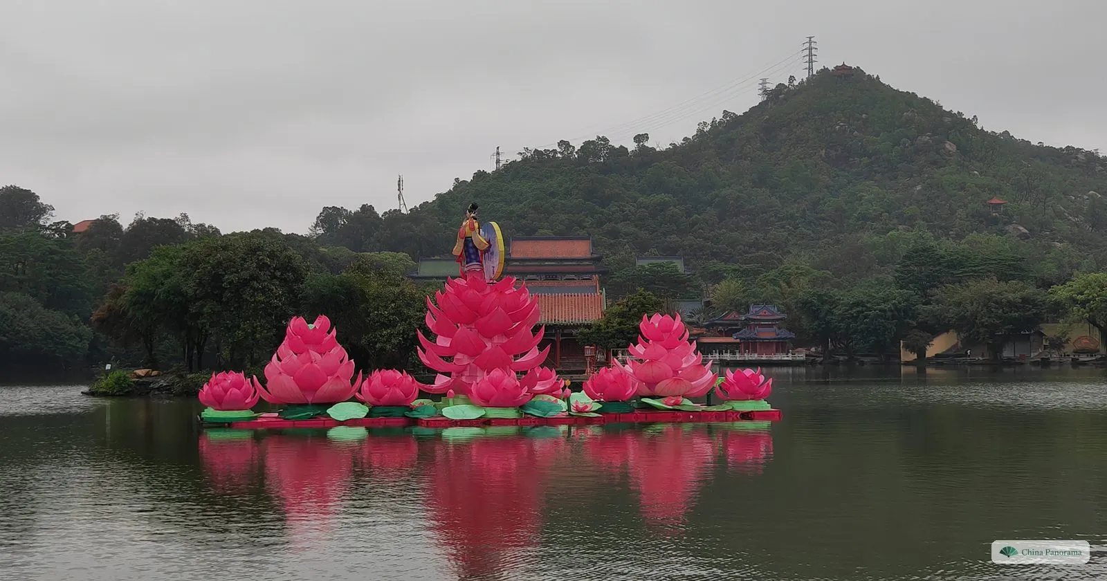 Giant pink lotus-flower lanterns floating on the lake of the New Yuanming Palace, with a hall and a wooded hill behind