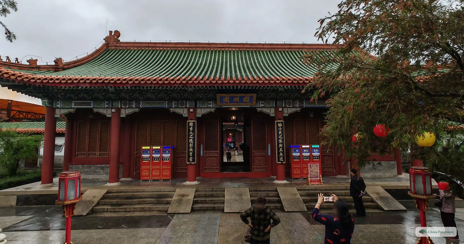 A hall with a green glazed roof and a blue plaque reading 圆明园, vertical boards with calligraphy on both sides of the door and visitors taking photographs