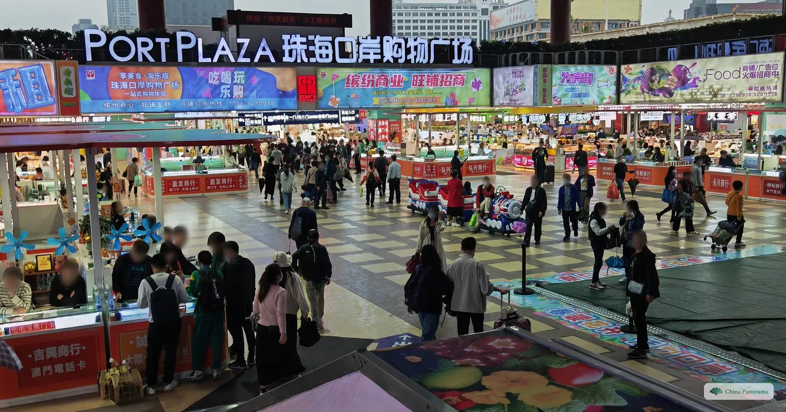 a crowded underground shopping hall seen from a staircase, with red counters selling phone cards and a big illuminated sign over the far end