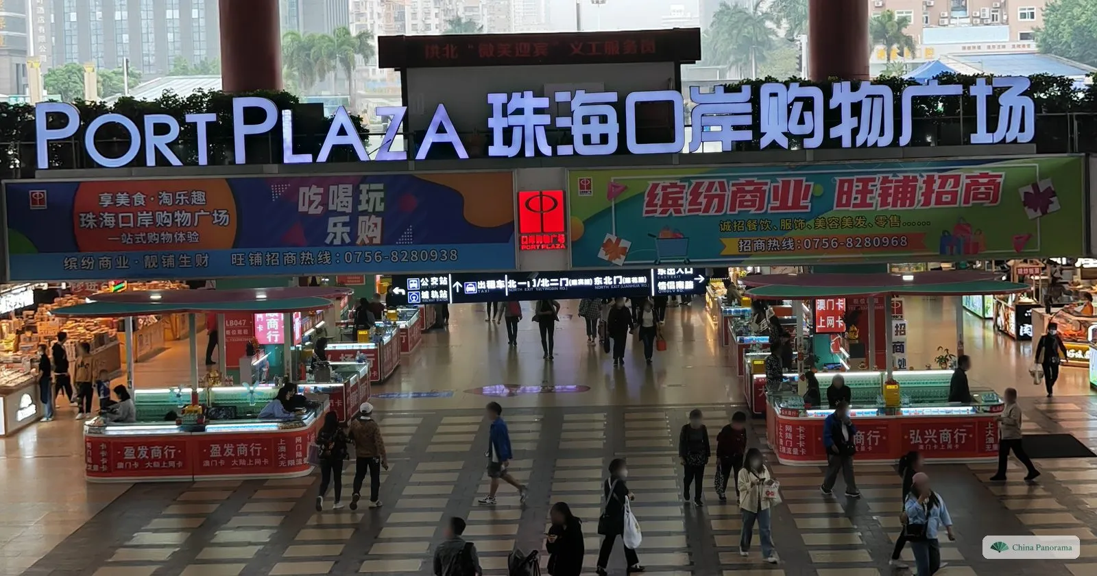 An underground shopping hall seen from above, under a big illuminated sign “Port Plaza 珠海口岸购物广场”, with counters and people walking on a chequered floor